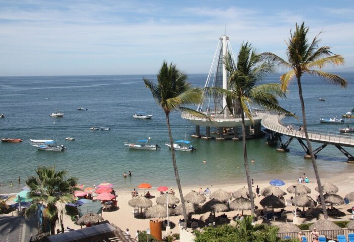 Beach view from Amapas Apartments, Puerto Vallarta. Pier, palm trees, boats, and beach umbrellas. Gay-friendly hotel in Puerto Vallarta.