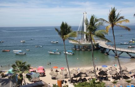 Beach view from Amapas Apartments, Puerto Vallarta. Pier, palm trees, boats, and beach umbrellas. Gay-friendly hotel in Puerto Vallarta.
