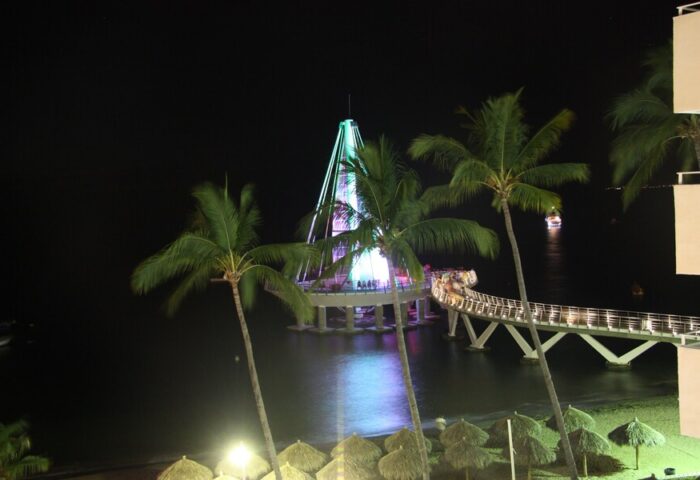 Night view from Amapas Apartments, Puerto Vallarta. Lit pier, palm trees, and beach umbrellas. Gay-friendly hotel in a vibrant travel destination.