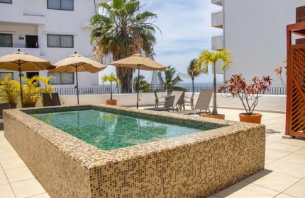 Rooftop pool at Amapas Apartments, a gay-friendly hotel in Puerto Vallarta. Lounge chairs, umbrellas, and palm trees offer a relaxing vacation vibe.