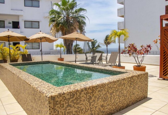 Rooftop pool at Amapas Apartments, a gay-friendly hotel in Puerto Vallarta. Lounge chairs, umbrellas, and palm trees offer a relaxing vacation vibe.