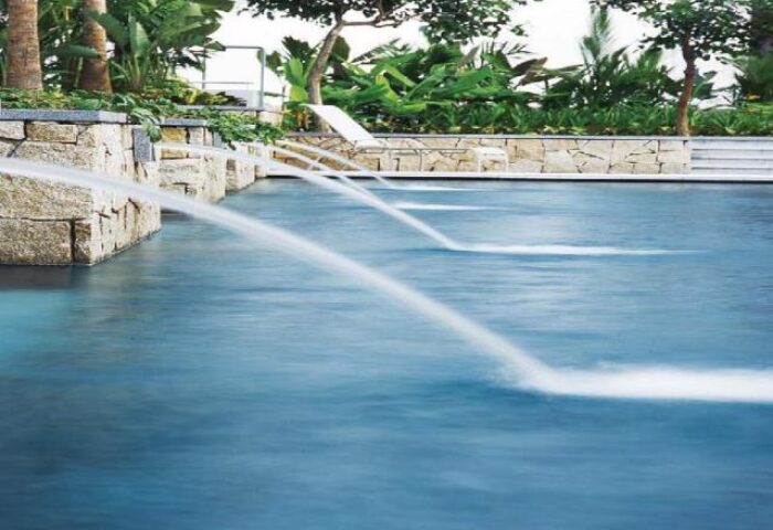 Amara Singapore gay-friendly hotel pool with water features. Lush greenery surrounds the pool area, creating a relaxing atmosphere.