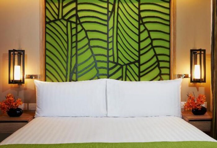 Amari Koh Samui gay-friendly hotel room. Bed with green leaf headboard, lamps, and flowers. A relaxing space for gay travelers.
