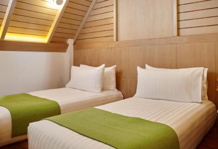 Amari Koh Samui gay-friendly hotel room. Twin beds with green throws, white linens, and wood paneling. Ideal for gay travelers.