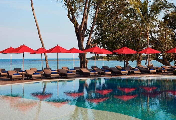 Amari Koh Samui gay-friendly hotel pool. Red umbrellas and loungers by the pool, ocean view. A luxurious gay travel destination.