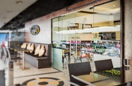 Entrance of Ambiance Pattaya Hotel, a gay-friendly hotel. Outdoor seating area with tables and chairs. Glass doors lead to the accommodation.