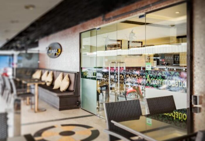 Entrance of Ambiance Pattaya Hotel, a gay-friendly hotel. Outdoor seating area with tables and chairs. Glass doors lead to the accommodation.
