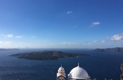 Amelot Art Suites gay-friendly hotel view. Santorini island vista with a church dome, blue sea, and clear sky. A travel destination.