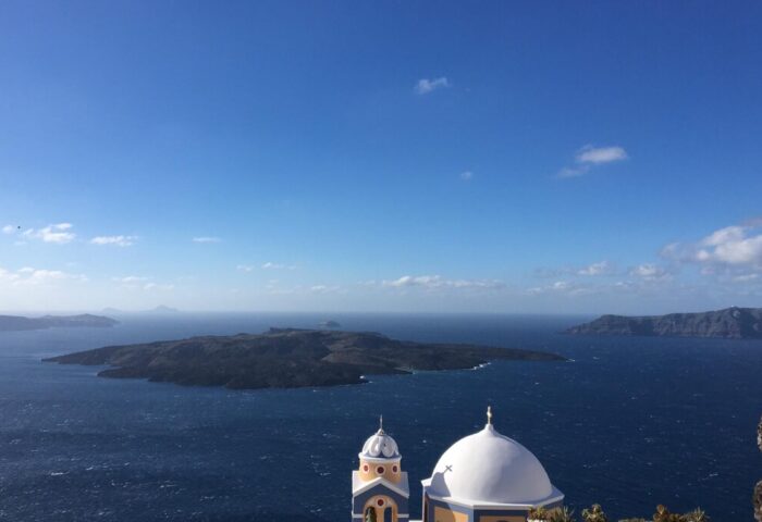 Amelot Art Suites gay-friendly hotel view. Santorini island vista with a church dome, blue sea, and clear sky. A travel destination.