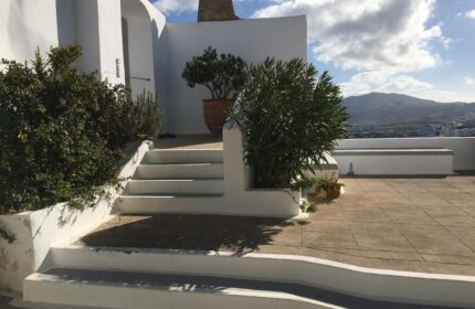 Amelot Art Suites gay-friendly hotel. Exterior view of white building with stairs, plants, and mountain backdrop. Ideal for gay travel.