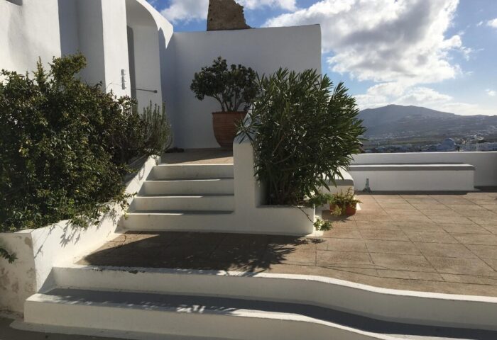 Amelot Art Suites gay-friendly hotel. Exterior view of white building with stairs, plants, and mountain backdrop. Ideal for gay travel.
