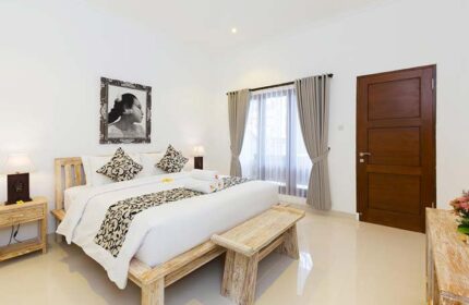 Amerta Seminyak gay-friendly hotel room. Bedroom with bed, bench, bedside table, lamp, curtains, and picture. Gay travel advice in Bali.