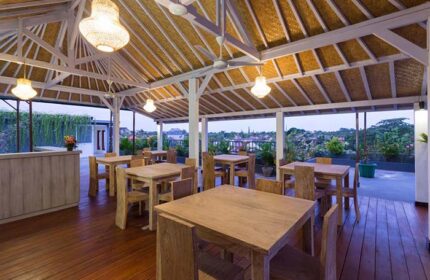 Amerta Seminyak, a gay-friendly hotel: Outdoor dining area with wooden tables and chairs under a traditional Balinese roof. Tropical view.