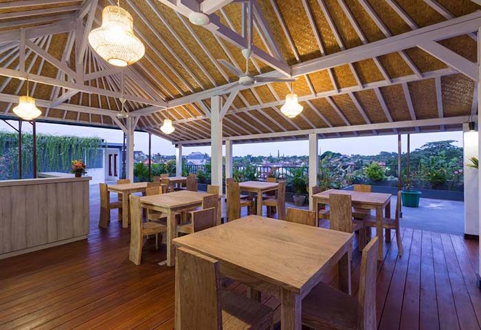 Amerta Seminyak, a gay-friendly hotel: Outdoor dining area with wooden tables and chairs under a traditional Balinese roof. Tropical view.