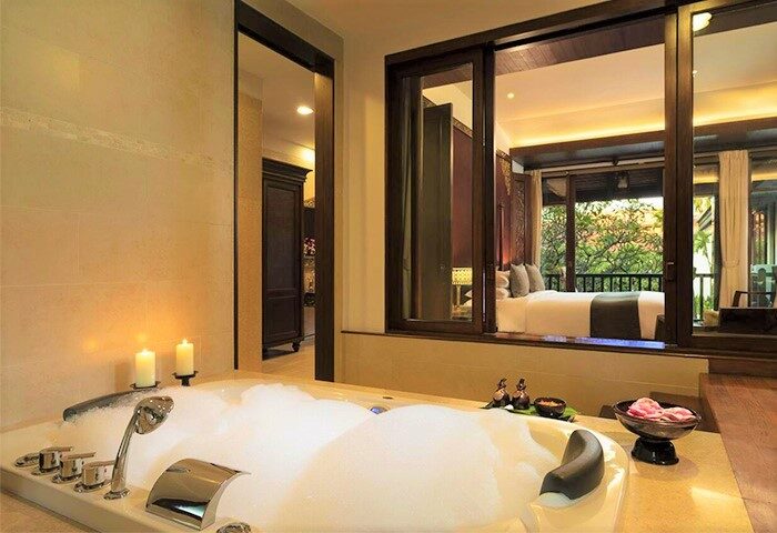 Luxurious bathroom at Anantara Angkor Resort, a gay-friendly hotel. Bubbles fill the tub, candles glow, and a balcony bedroom beckons.