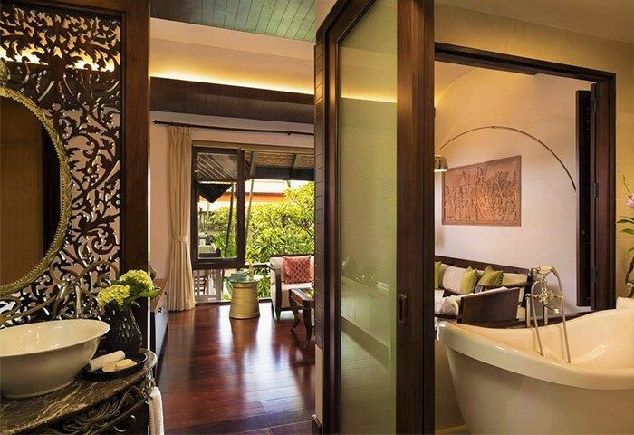 Anantara Angkor Resort bathroom and living area. Gay-friendly hotel with luxury bathtub, carved mirror, wood floors, and outdoor balcony.
