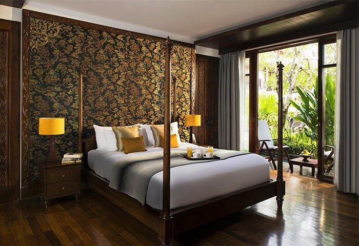 Bedroom at the gay-friendly Anantara Angkor Resort. Four-poster bed, dark wood floors, and a balcony overlooking lush greenery. Luxury travel.