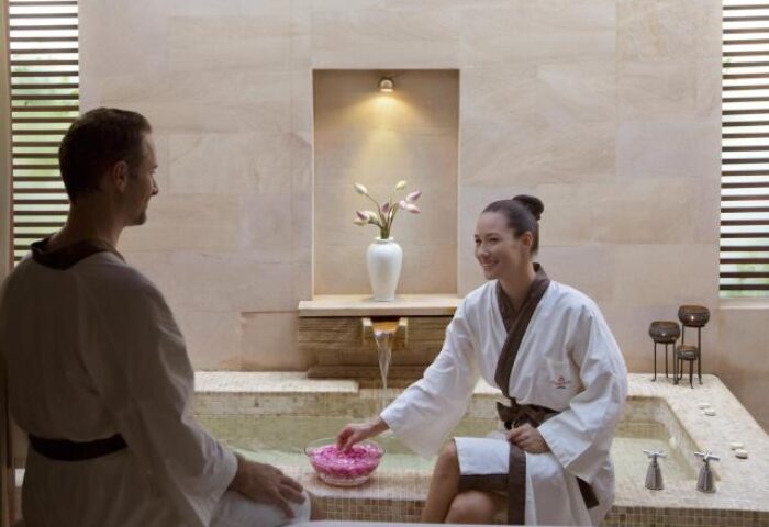 Gay-Friendly Hotel Anantara Angkor Resort spa. A man and woman in robes relax by a bath with rose petals. Luxury travel for gay men.