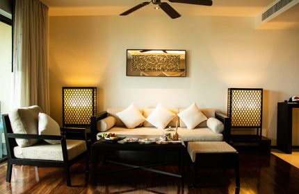 Anantara Bophut Koh Samui Resort suite interior. Gay-friendly hotel living room with sofa, chair, and dark wood furniture. Tropical decor.