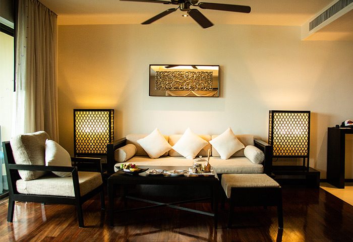 Anantara Bophut Koh Samui Resort suite interior. Gay-friendly hotel living room with sofa, chair, and dark wood furniture. Tropical decor.