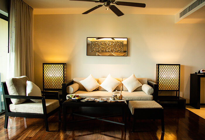 Anantara Bophut Koh Samui Resort suite interior. Gay-friendly hotel living room with sofa, chair, and dark wood furniture. Tropical decor.