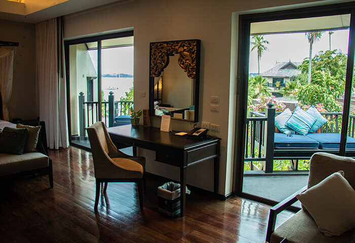 Anantara Bophut Koh Samui Resort room interior. Desk with mirror, chair, and balcony with daybed. Gay-friendly hotel stay in Thailand.