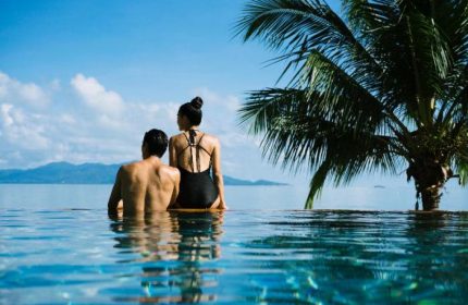 Couple at Anantara Bophut Koh Samui Resort's infinity pool, palm tree, sea view. Gay-friendly hotel for a luxurious vacation.