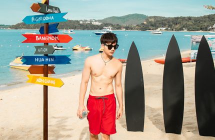 Gay-friendly Anantara Bophut Koh Samui Resort: Man on the beach with surfboards and destination signpost. Thailand travel for gay men.