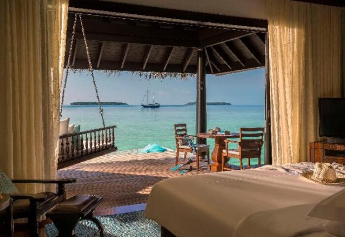 Anantara Kihavah Maldives Villas gay-friendly hotel room. Ocean view with swing, table, and chairs on the deck. Sailboat in the distance.
