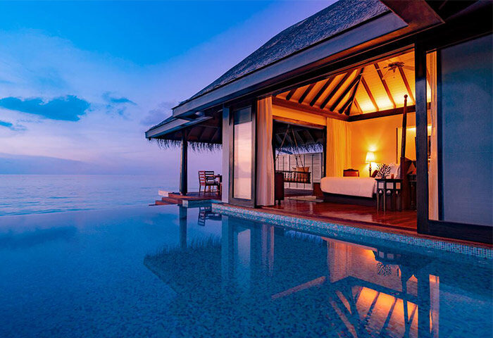 Gay-friendly Anantara Kihavah Maldives Villas: Overwater bungalow with infinity pool at dusk. Luxury travel for gay men in the Maldives.