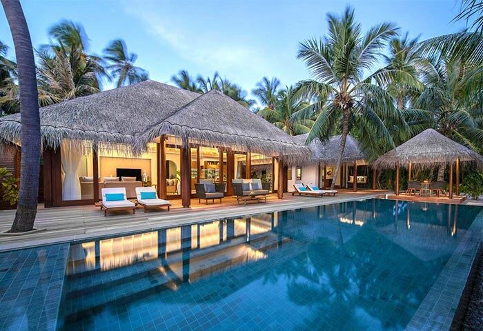 Gay-Friendly Anantara Kihavah Maldives Villas: Thatched-roof villa with private pool. Palm trees and lounge chairs. Luxury travel.