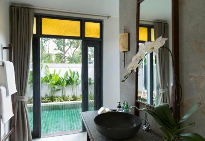 Bathroom at Anantara Lawana Koh Samui Resort, a gay-friendly hotel. Sink, orchid, and window view of pool. Ideal for gay travel.