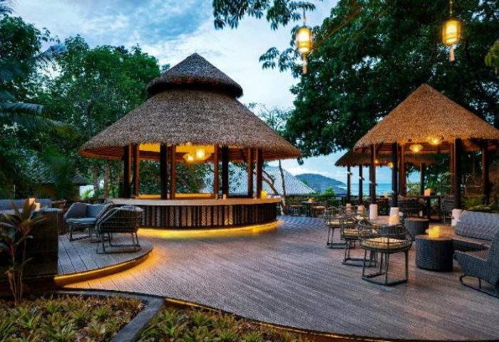 Anantara Lawana Koh Samui Resort's outdoor bar area. Gay-friendly hotel with thatched roof structures and ambient lighting. Tropical island vibe.