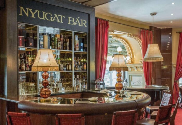 Nyugat Bar at Anantara New York Palace, Budapest. Gay-friendly, pet-friendly hotel bar with liquor bottles and lamps.