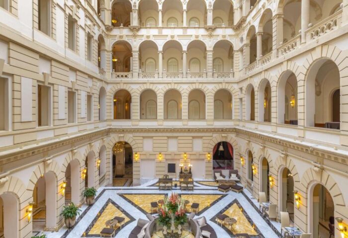 Anantara New York Palace Budapest's interior. Gay-friendly, pet-friendly hotel atrium view. Arches, marble floors, and seating areas.