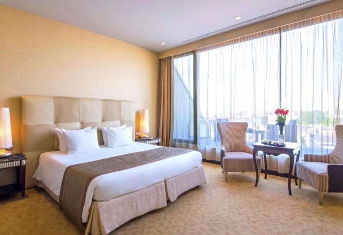 Anantara New York Palace Budapest bedroom. Gay-friendly, pet-friendly hotel room with large bed, chairs, and city view. Luxury stay.