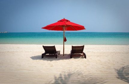 Beach chairs under a red umbrella at Anantara Rasananda Koh Phangan Villas. A gay-friendly hotel with a beautiful beach.