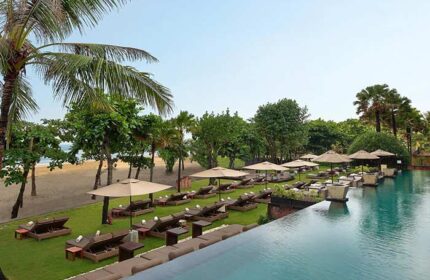 Anantara Seminyak Bali Resort pool view. Gay-friendly hotel with beach access, lounge chairs, umbrellas, and lush tropical greenery. Relaxing vacation.
