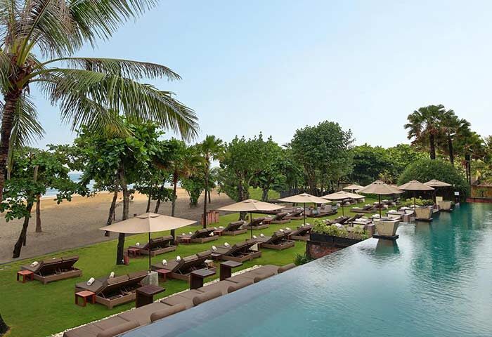 Anantara Seminyak Bali Resort pool view. Gay-friendly hotel with beach access, lounge chairs, umbrellas, and lush tropical greenery. Relaxing vacation.