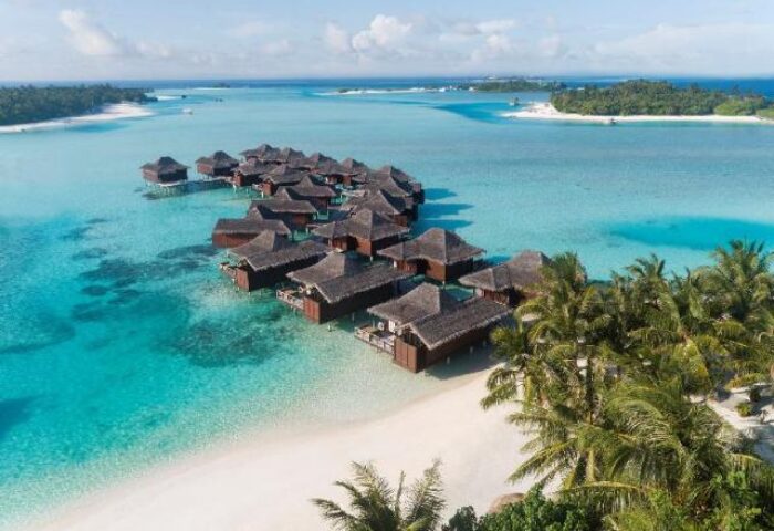 Aerial view of Anantara Veli Maldives Resort, a gay-friendly hotel. Overwater bungalows, turquoise water, white sand beach, and palm trees.