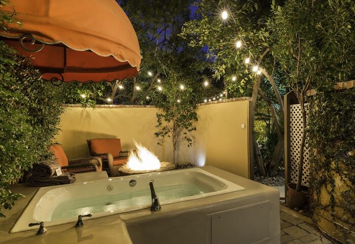 Gay-friendly Andalusian Court Hotel outdoor jacuzzi and fire pit. Lush trees and string lights create a romantic atmosphere.