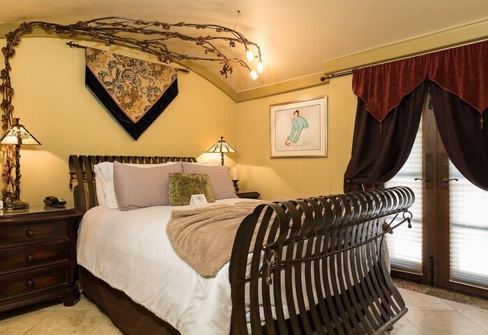 Andalusian Court gay-friendly hotel room. Ornate metal bed frame, artistic wall decor, and warm lighting create a luxurious ambiance. Perfect for gay travel.