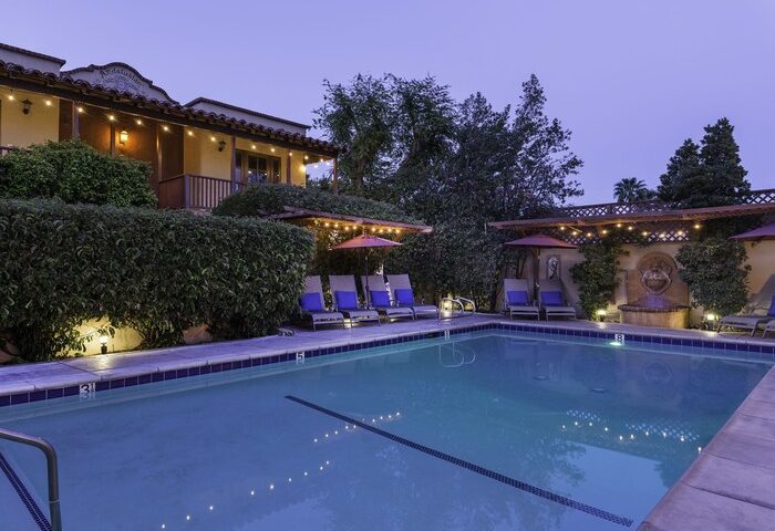 Andalusian Court gay-friendly hotel pool at dusk. Lounge chairs, umbrellas, and lush greenery surround the pool, creating a relaxing ambiance.