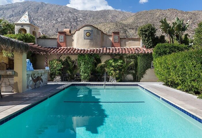 Andalusian Court gay-friendly hotel swimming pool. Lush greenery, Spanish-style architecture, and mountain backdrop. Ideal gay travel destination.