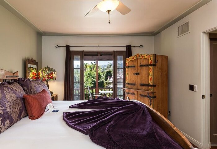 Andalusian Court gay-friendly hotel room. Bedroom with balcony, ceiling fan, wooden closet, and plush purple bedding. A great gay travel destination.