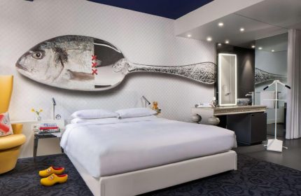 Andaz Amsterdam Prinsengracht gay-friendly hotel room. Bed with a fish/spoon mural, clogs, and bathroom. Luxury travel for gay men.