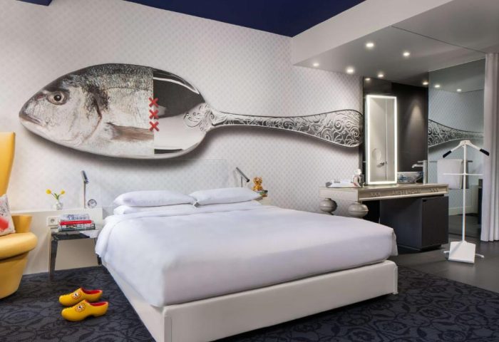 Andaz Amsterdam Prinsengracht gay-friendly hotel room. Bed with a fish/spoon mural, clogs, and bathroom. Luxury travel for gay men.