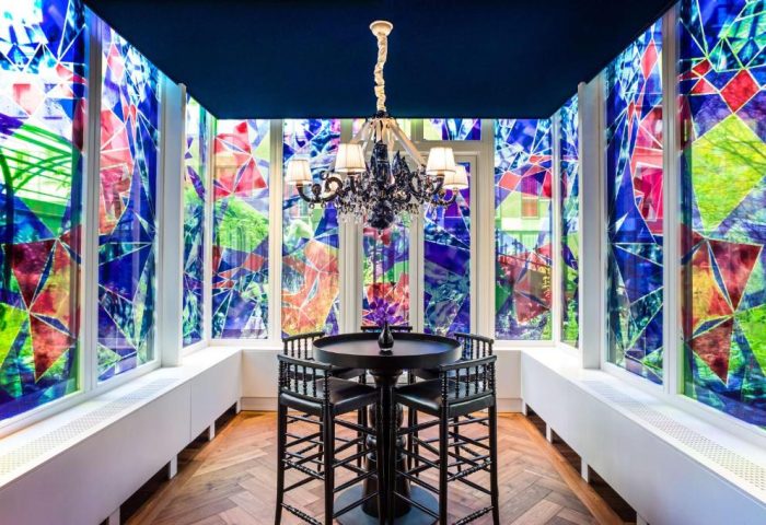 Andaz Amsterdam Prinsengracht gay-friendly hotel: Room with colorful geometric window art, black table and chairs, and chandelier.