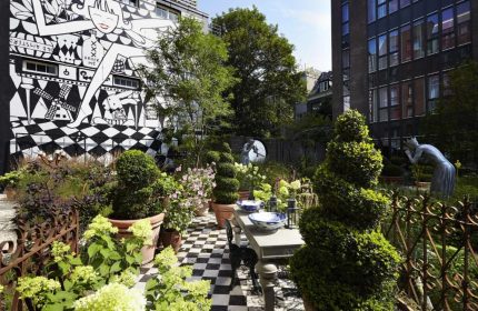 Andaz Amsterdam Prinsengracht garden. Gay-friendly hotel with black and white mural, checkered floor, topiary, table setting, and sculptures.