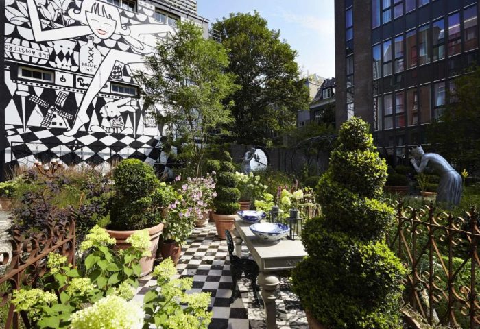 Andaz Amsterdam Prinsengracht garden. Gay-friendly hotel with black and white mural, checkered floor, topiary, table setting, and sculptures.